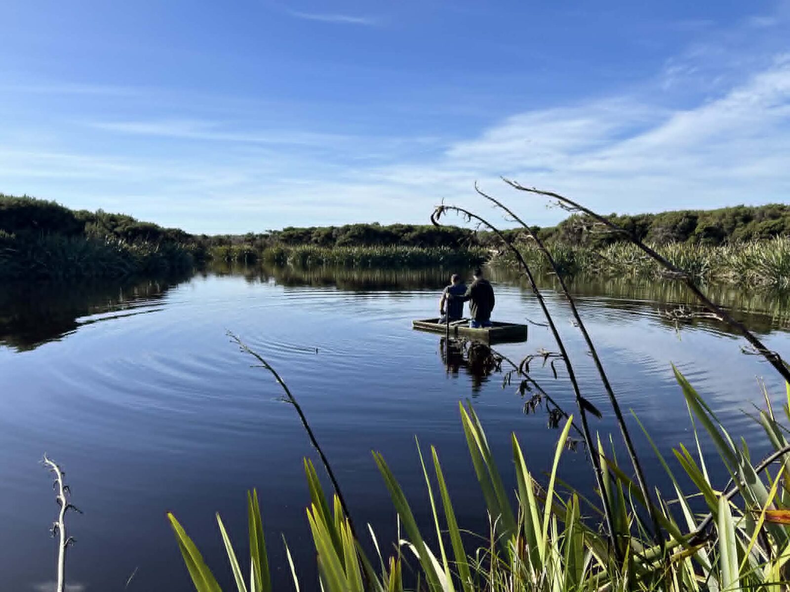 Two hunters heading out across the lake in a flat-bottomed boat at dawn for a day of duck hunting in New Zealand